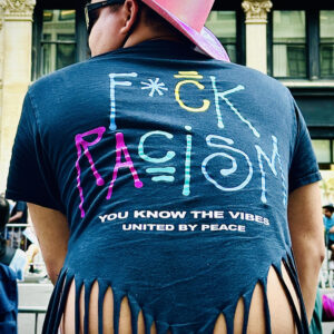 Woman sitting in front of a crowd in the streets, wearing a shirt with fuck racism written on it